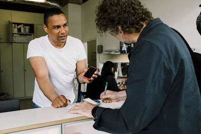 Mature repairman showing broken smart phone to customer doing paperwork at store