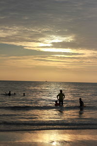 Silhouette people swimming in sea against sky during sunset