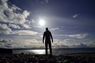 Full length of man standing on pebble shore at beach against sky during sunny day