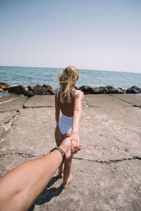 Cropped image of man holding woman hand at beach during sunny day