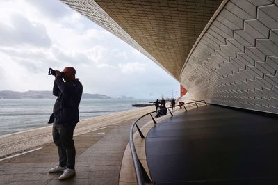 People photographing by sea against sky