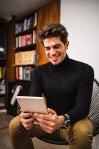 Young man using mobile phone while sitting on laptop