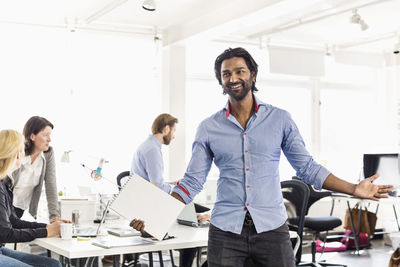 Mid adult businessman standing with arms outstretched in office