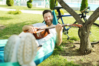 Smiling man playing guitar lying on hammock