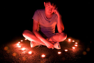 Man with closed eyes sitting amidst lit diya in darkroom