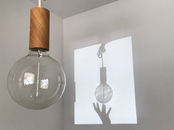 Optical illusion of shadow holding light bulb on white wall