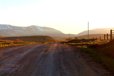 Road leading towards mountains against clear sky