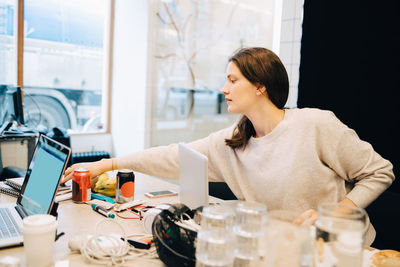 Young female computer programmer working while sitting at desk in small creative office