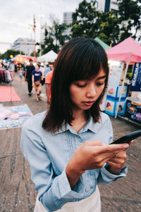 Woman using phone while standing on footpath