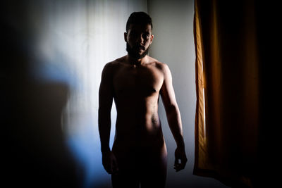 Full length of shirtless man standing against wall at home