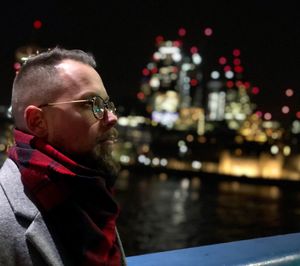 Portrait of man wearing sunglasses against illuminated city at night