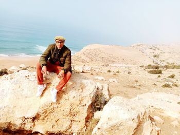 Man sitting on rock at beach against sky