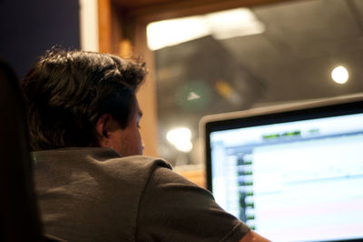 Rear view of man using computer in illuminated recording studio