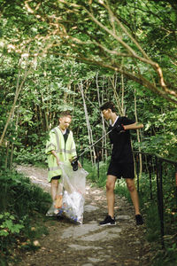 Full length of boys collecting garbage on bag amidst plants