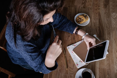 From above of pensive female freelancer sitting at table in cafe and using tablet while working on startup project