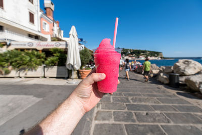 Midsection of person holding drink against built structure