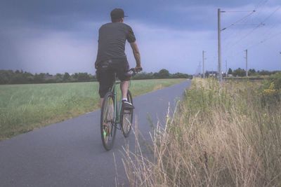 Rear view of man riding bicycle on footpath