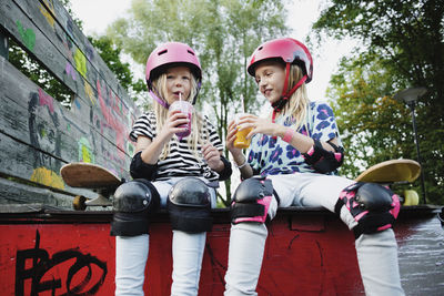 Smiling friends enjoying drink while sitting on edge of skateboard ramp