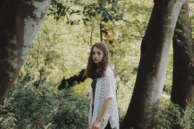 Portrait of woman standing by tree trunk in forest