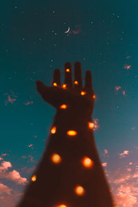 Close-up of illuminated hand against sky at night