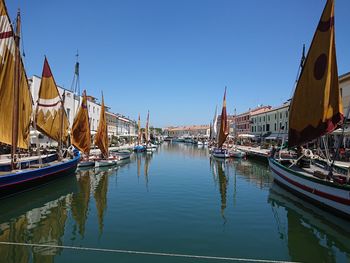 Sailboats moored in harbor against sky in city