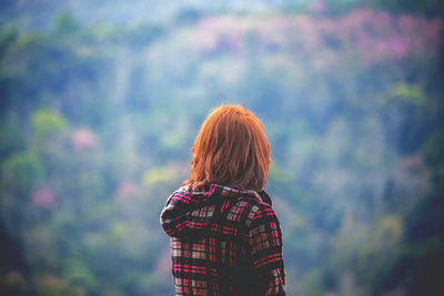 Rear view of young woman standing against trees in forest