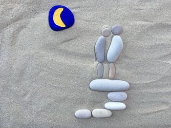 Directly above view of moon drawing on pebble at sandy beach