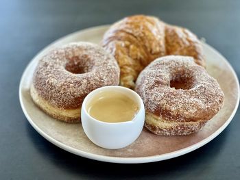 Close-up of cinnamon cronuts, croissant and cup of coffee on plate on table.