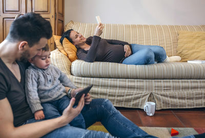 Mother holding mobile phone while father with son using digital tablet in living room