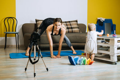 Young mother fitness instructor personal trainer record video near camera at home with baby
