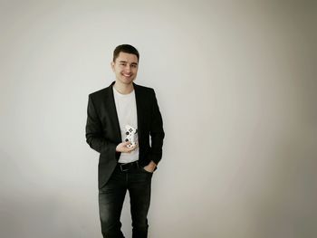 Portrait of smiling man holding remote while standing against gray background