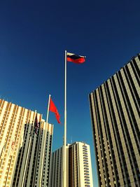 Low angle view of flag against buildings against clear blue sky