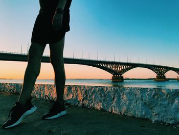 Low section of man standing on bridge over river against sky