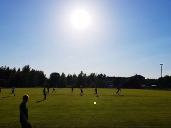 People playing soccer against sky on sunny day