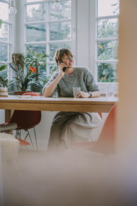 Mid adult woman talking on smart phone while sitting at home