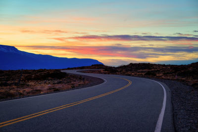 Empty road along landscape at sunset