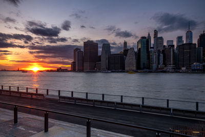 Sea by city buildings against sky during sunset