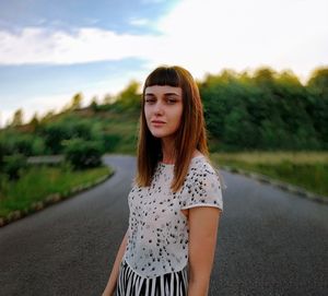 Portrait of beautiful young woman standing on road against sky