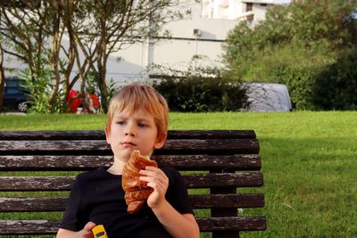 A   boy with a croissant in his hand looks thoughtfully into the distance. a tired five-year-old boy