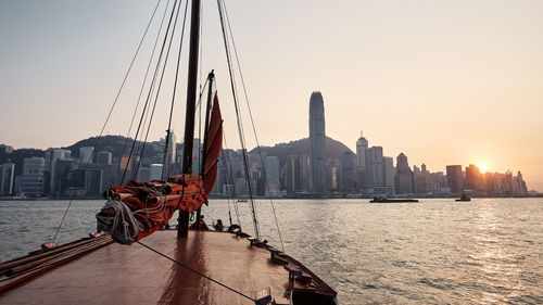 Traditional junk boat crossing victoria harbour against hong kong skyline at sunset.