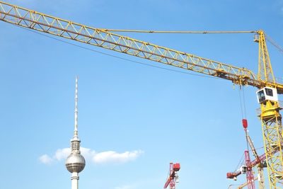 Low angle view of fernsehturm and cranes against sky