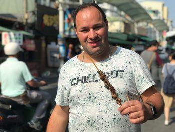 Portrait of mid adult man eating while standing on street in city