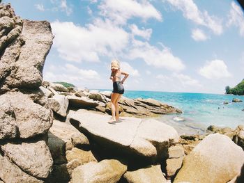 Man standing on rock by sea against sky