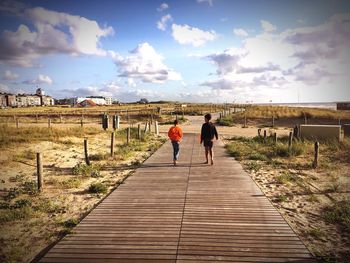 Rear view full length of boys walking on boardwalk at beach