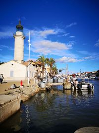 Lighthouse amidst sea and buildings against sky