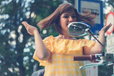 Portrait of smiling young woman tossing hair while sitting on motor scooter