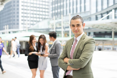 Portrait of smiling businessman standing against colleagues discussing on footpath 