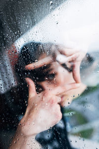 Close-up portrait of woman seen through wet window in rainy season