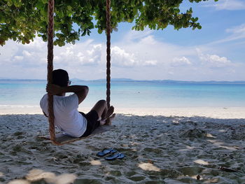 Rear view of man sitting on swing at beach