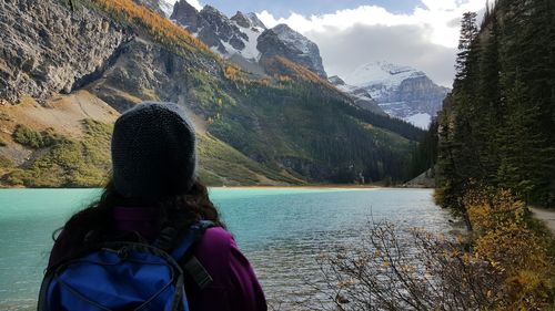 Rear view of woman standing by river against mountains